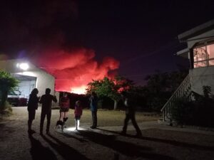 A few people are standing between two buildings in the dark with the sky lit up behind them due to a monster wildfire